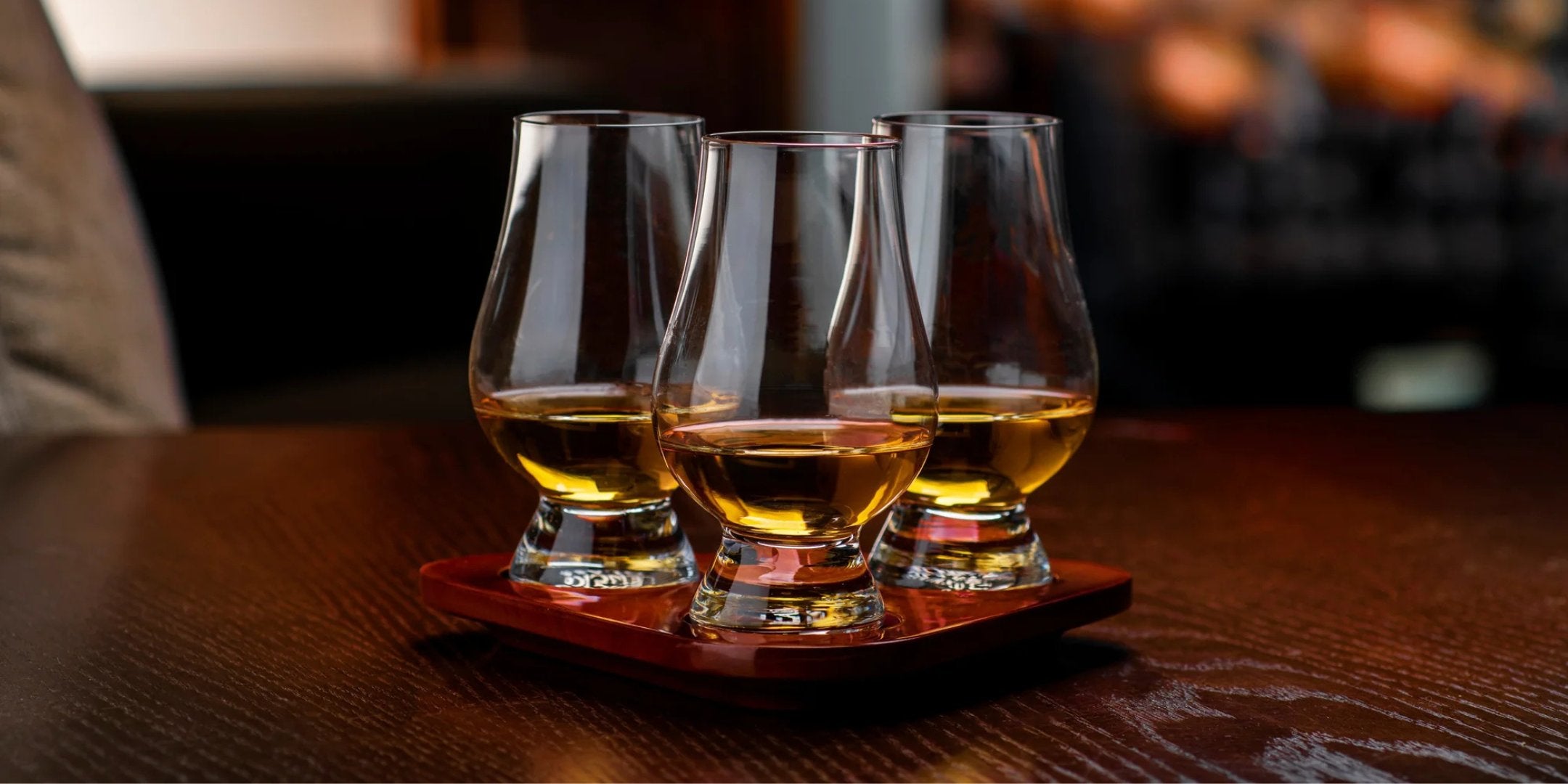Set von Glencairn Whiskygläsern auf einem Holztablett, gefüllt mit goldfarbenem Whisky