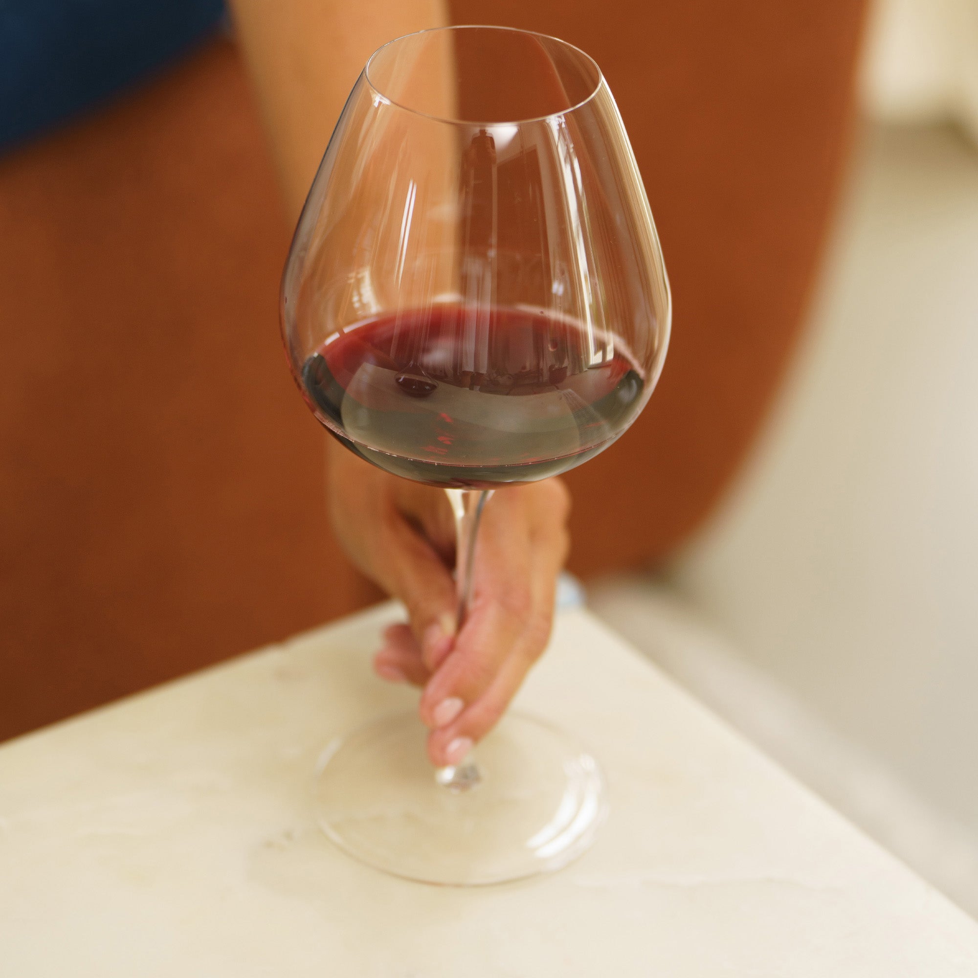 Eleganter Burgunderkelch Fino von Stölzle Lausitz mit Rotwein, gehalten von einer Hand auf einem Tisch