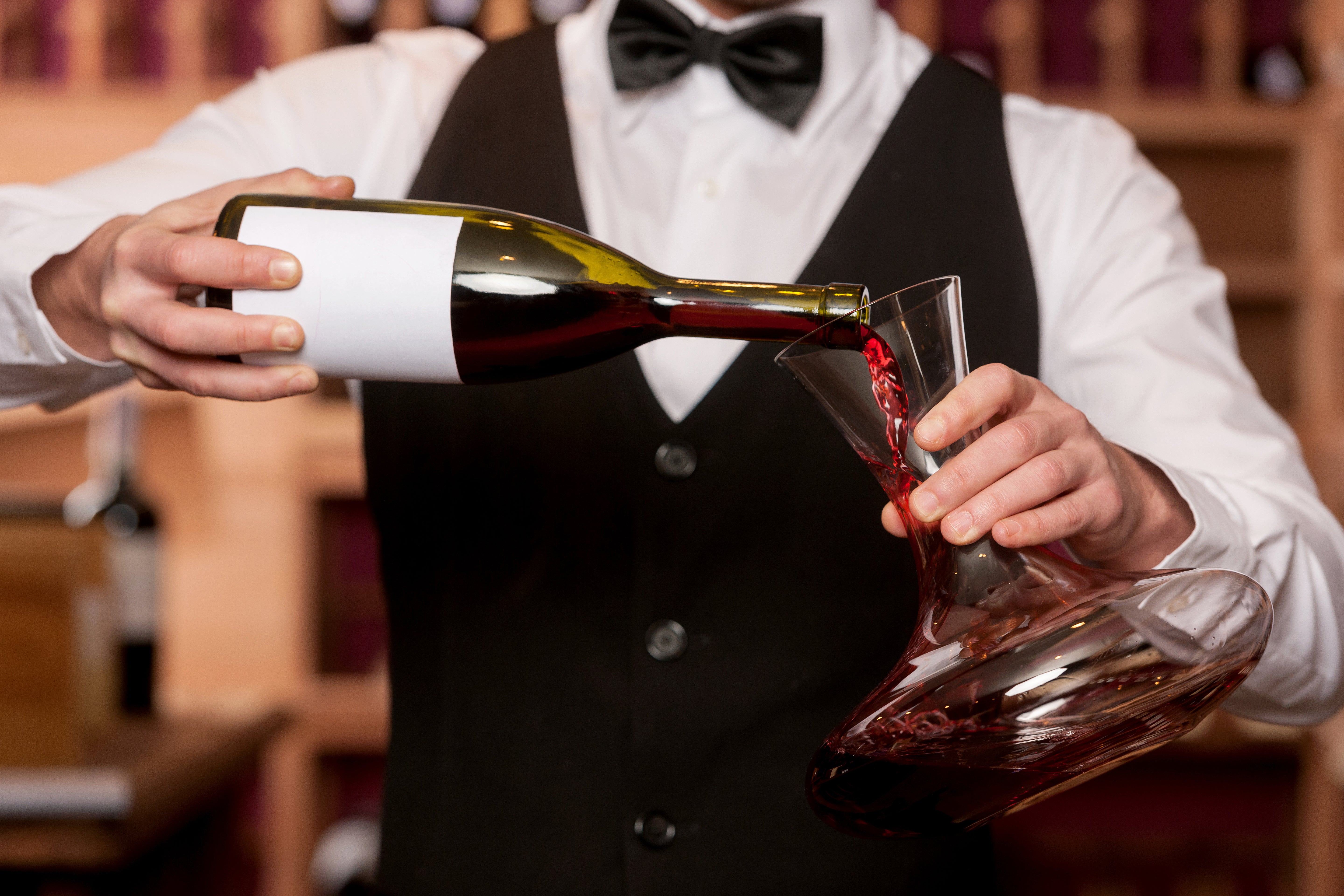 Ein Kellner gießt Rotwein aus einer Flasche in einen Dekanter Weinland kaufen für optimalen Genuss