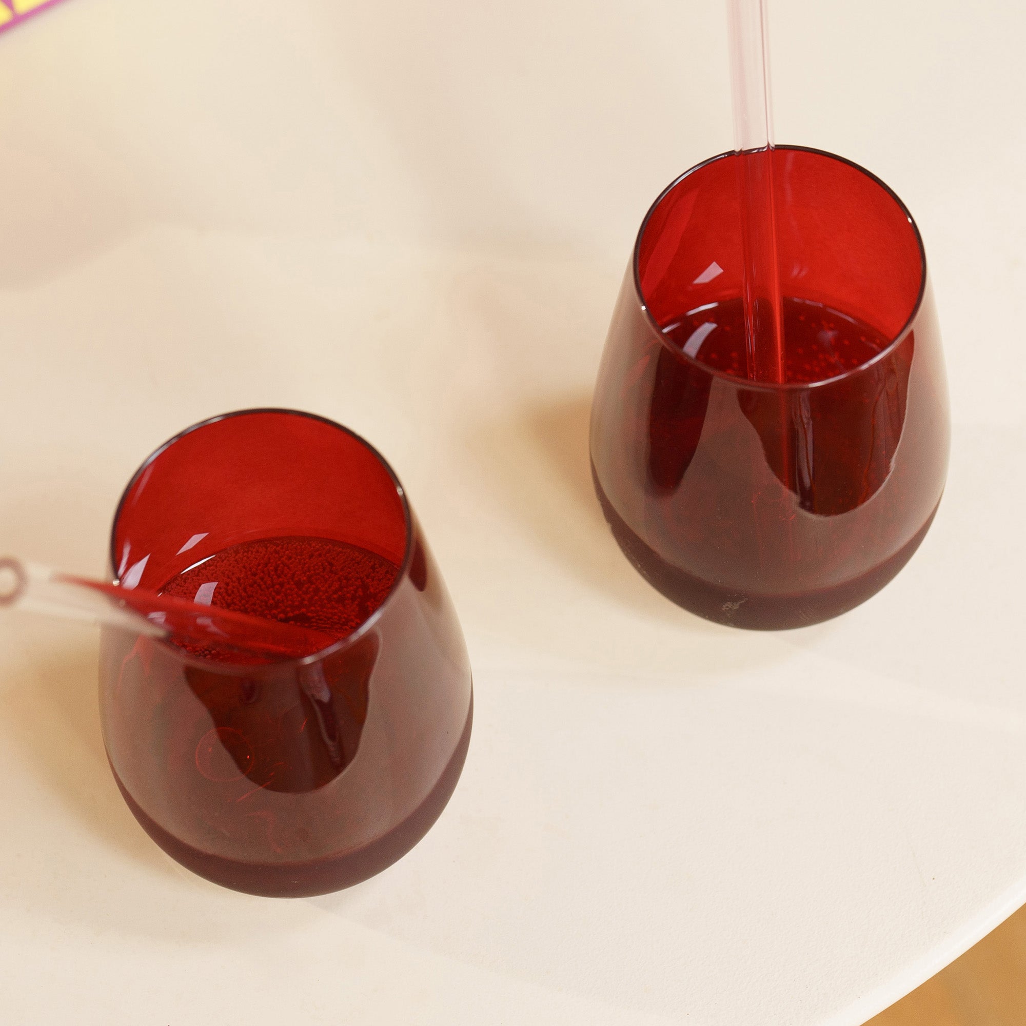Zwei rote, bauchige Farbige Gläser für Getränke mit Strohhalmen auf einem Tisch