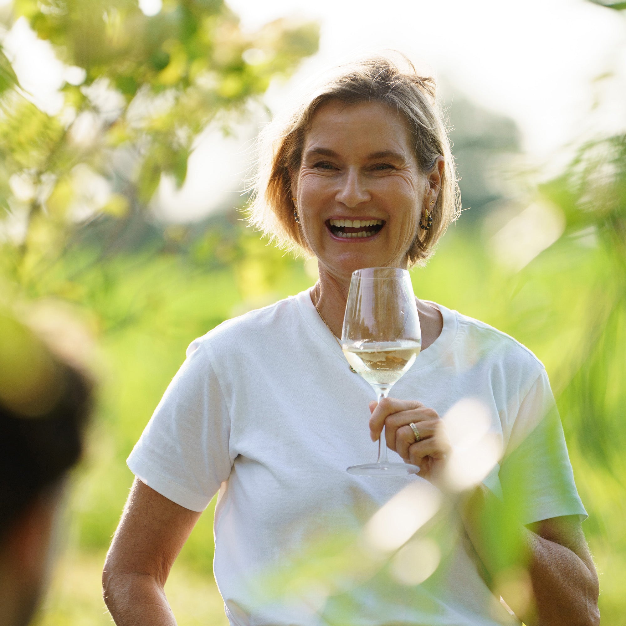 Frau mit funktionalen Weingläsern in der Natur, genießt weißen Wein und lacht glücklich