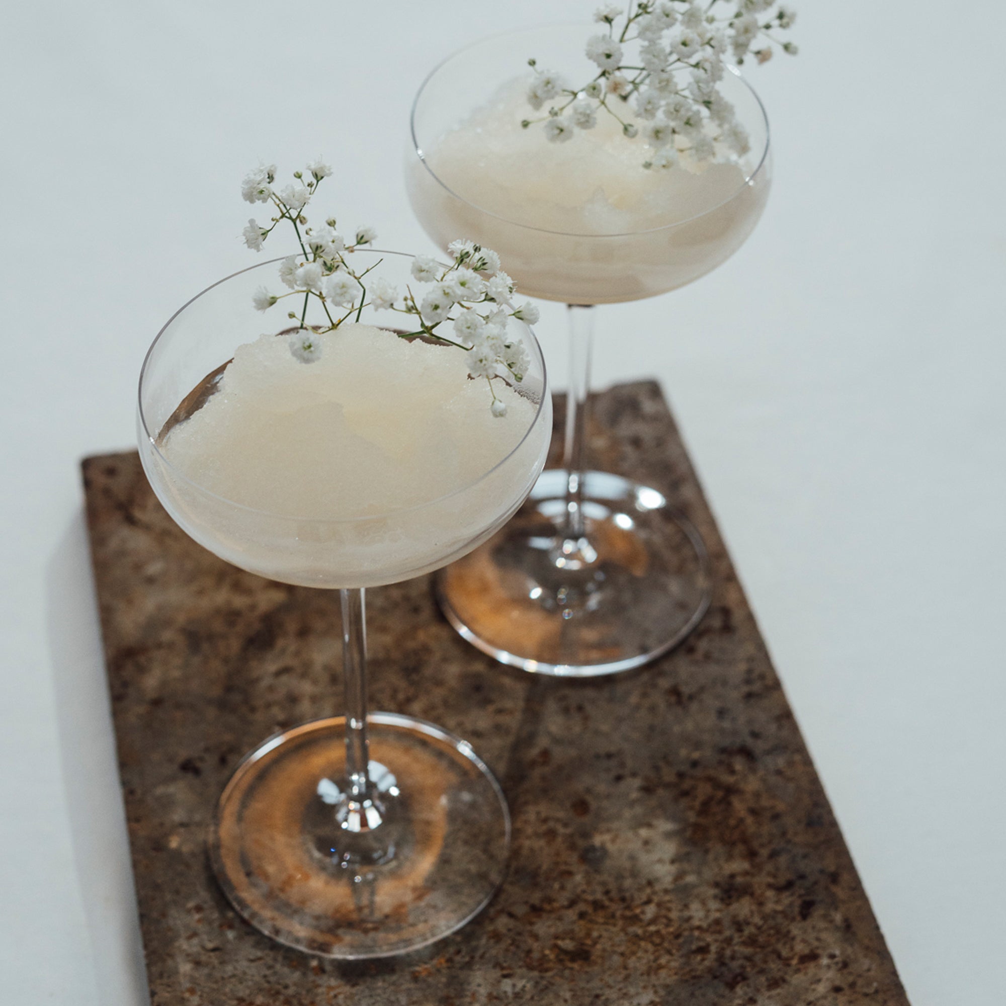 Zwei hochwertige Champagnerschalen mit Eis und Blumen auf einem rustikalen Tablett