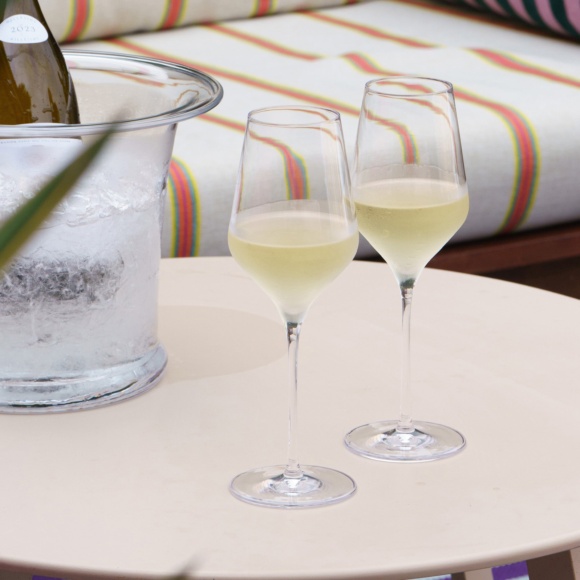 Zwei hochwertige Weißweingläser auf einem Tisch neben einer Kühlwanne mit Eis und Weinflasche