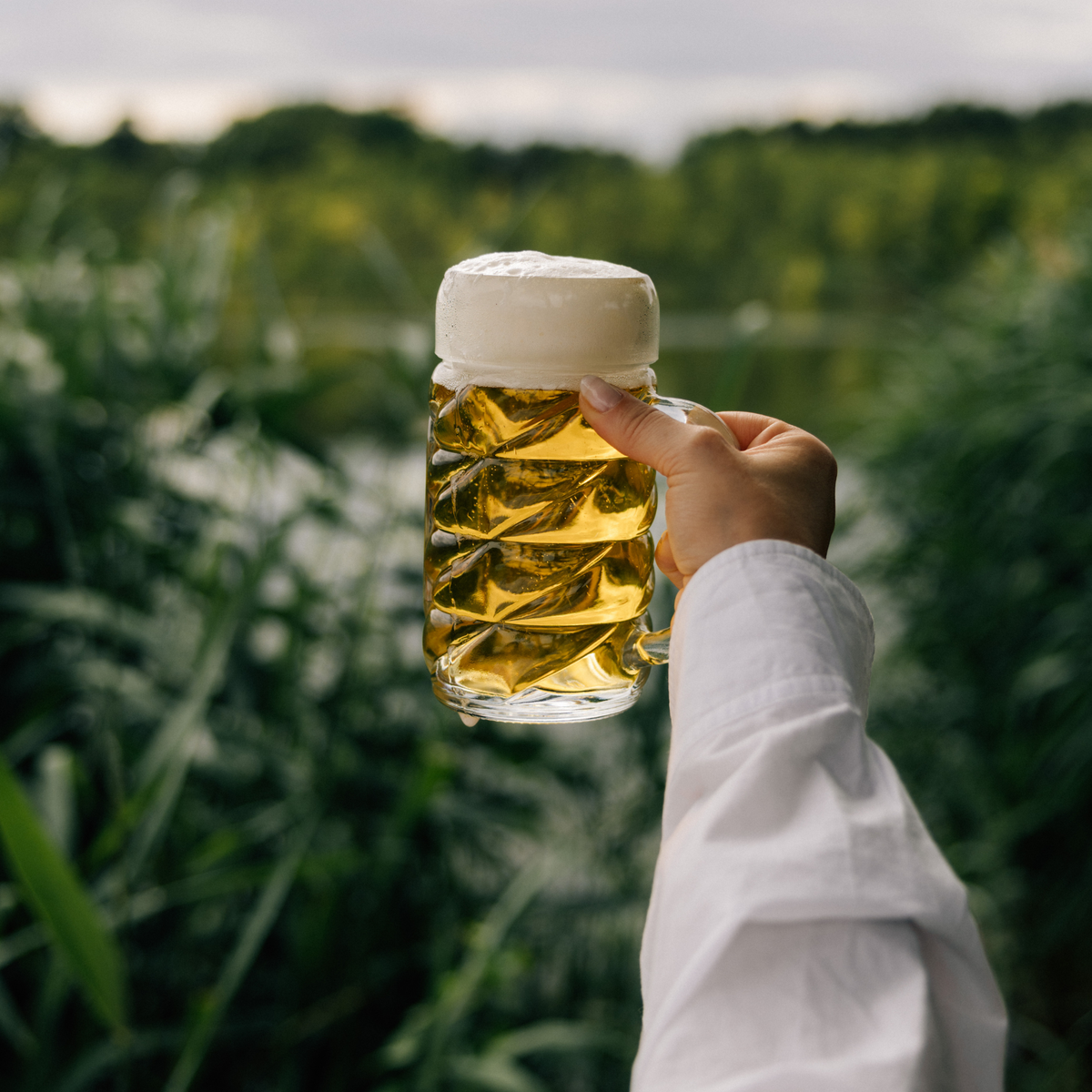 Oberglas Diamond Bierkrug mit Dekorfläche 1000ml, gefüllt mit tropfender Schaumkrone in der Natur, gehalten von einer Frauenhand