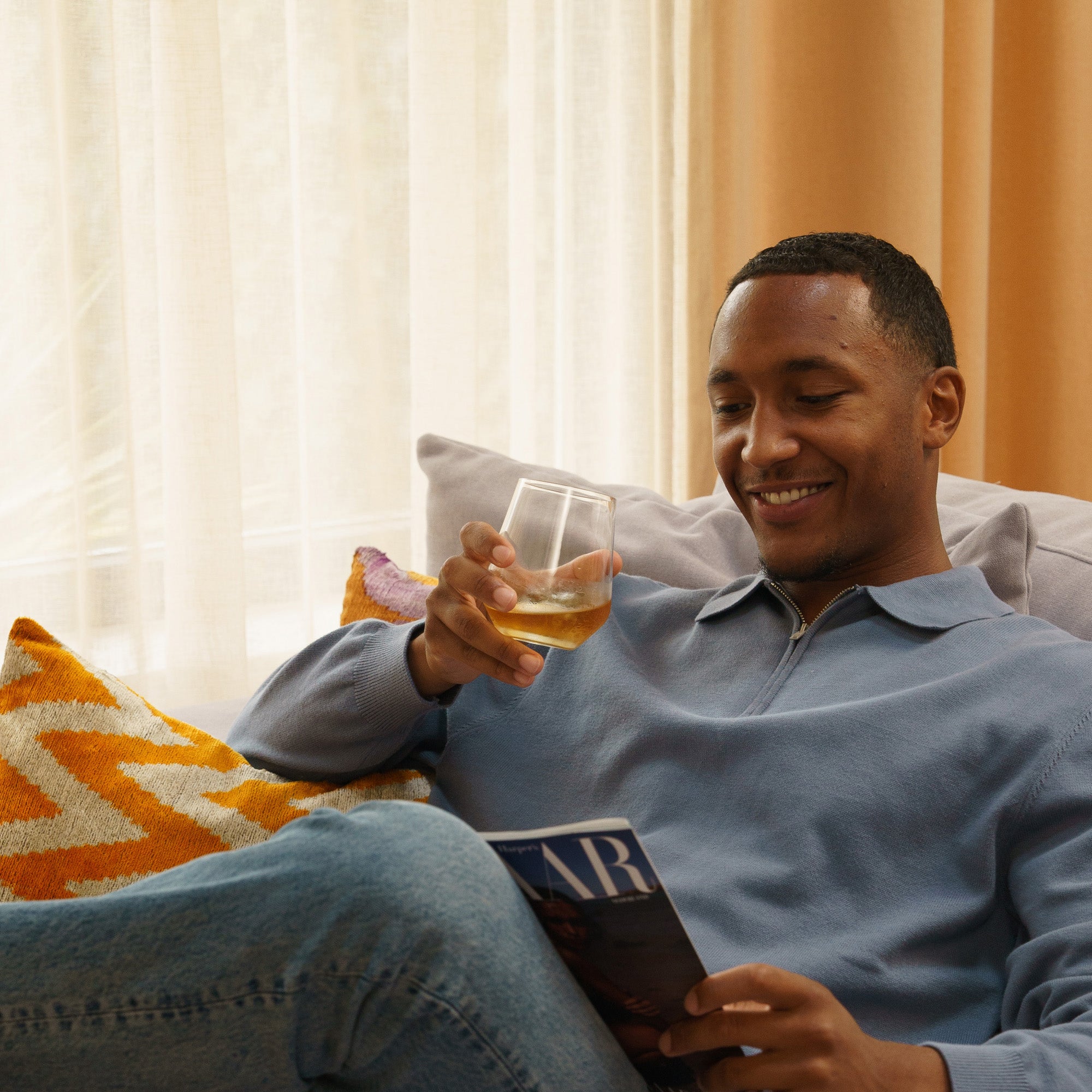 Mann entspannt mit einem Drink in Hand in einem modernen Raum, premium German whisky glasses auf dem Tisch