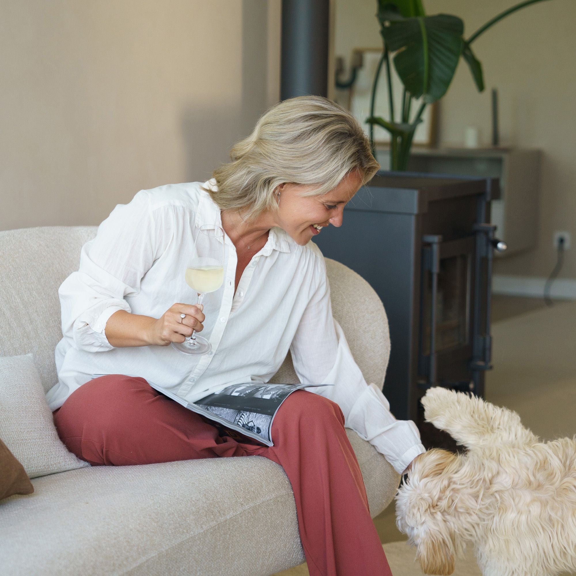 Frau genießt STARlight Champagnergläser auf der Couch mit Hund und Magazin in hellem Wohnzimmer