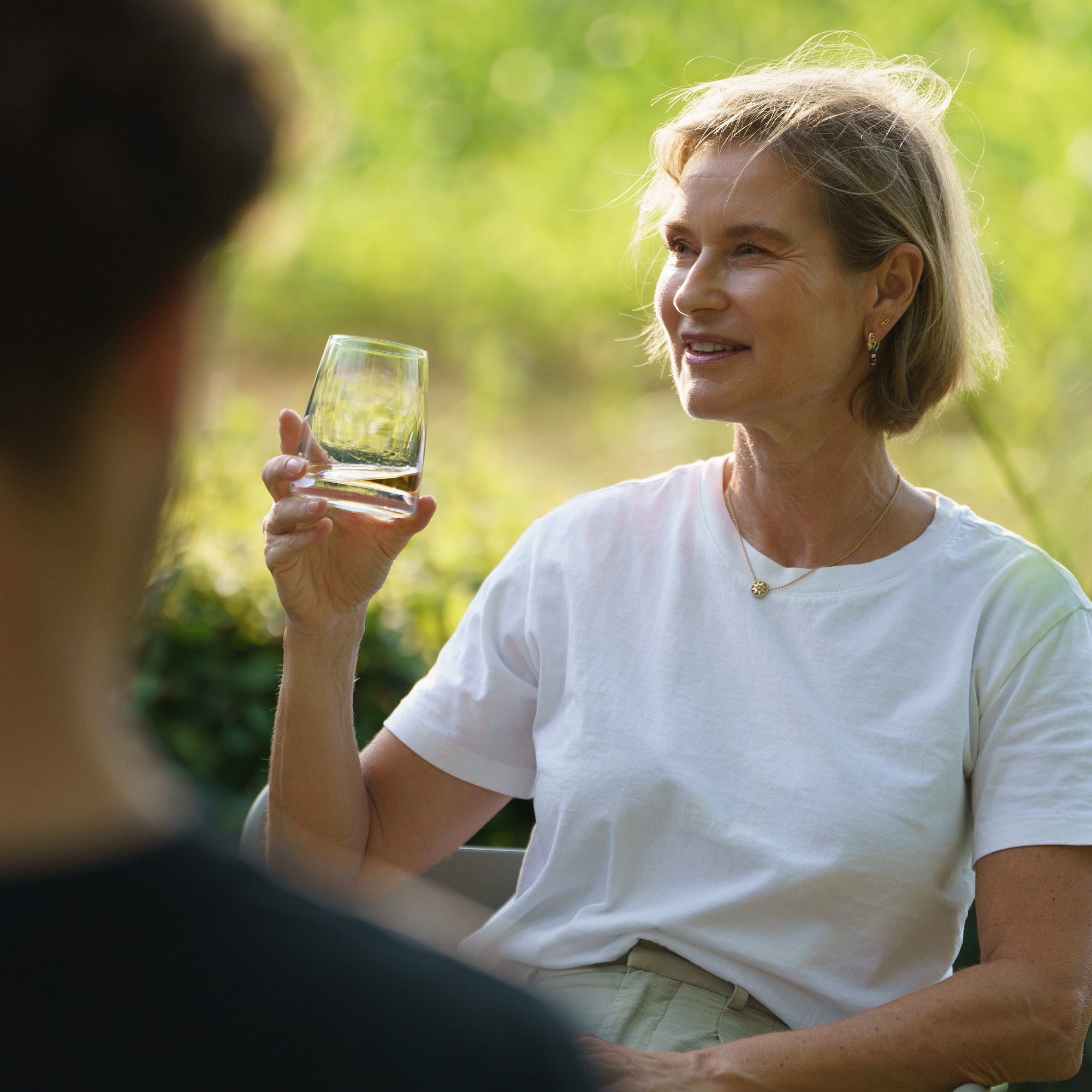 Eine Frau hält ein Glas in der Hand und genießt ihr Whisky D.O.F. Gläser Set in einer entspannten Außenumgebung