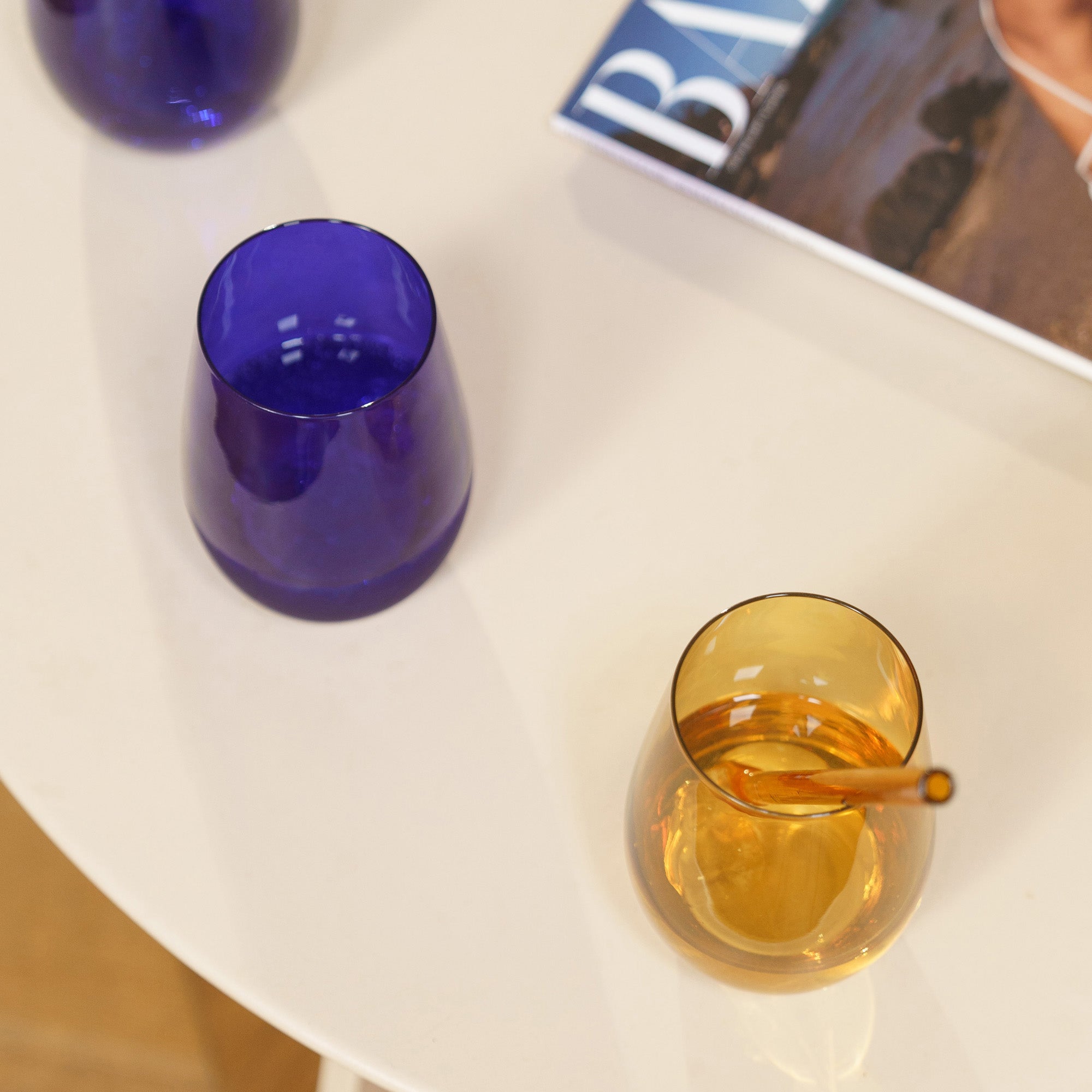 Bunte Gläser Made in Germany auf einem Tisch mit Zeitschrift und Cocktailrührer