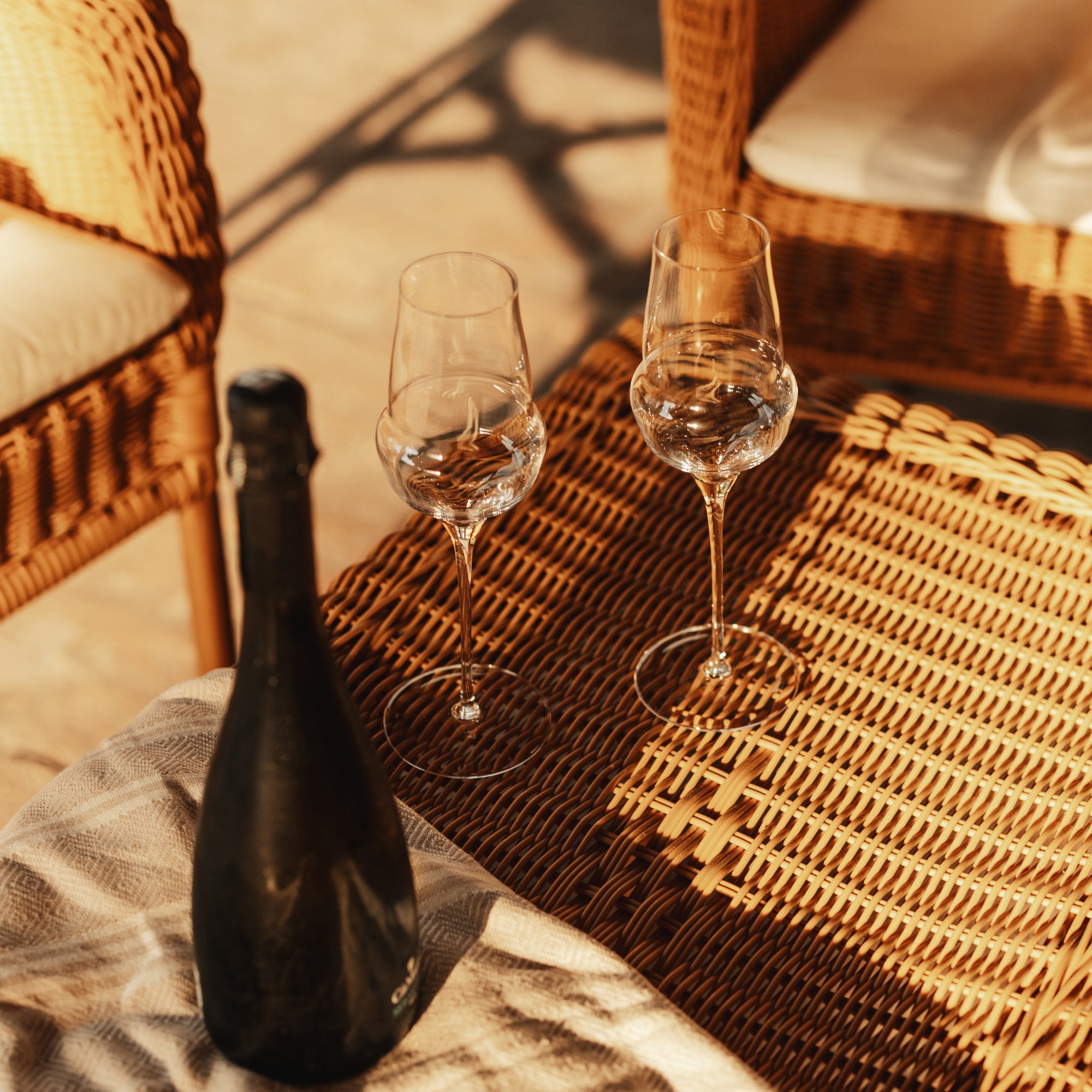 Zwei leere Champagnergläser auf einem Rattan-Tisch mit einer Flasche daneben hochwertige Champagnergläser kaufen