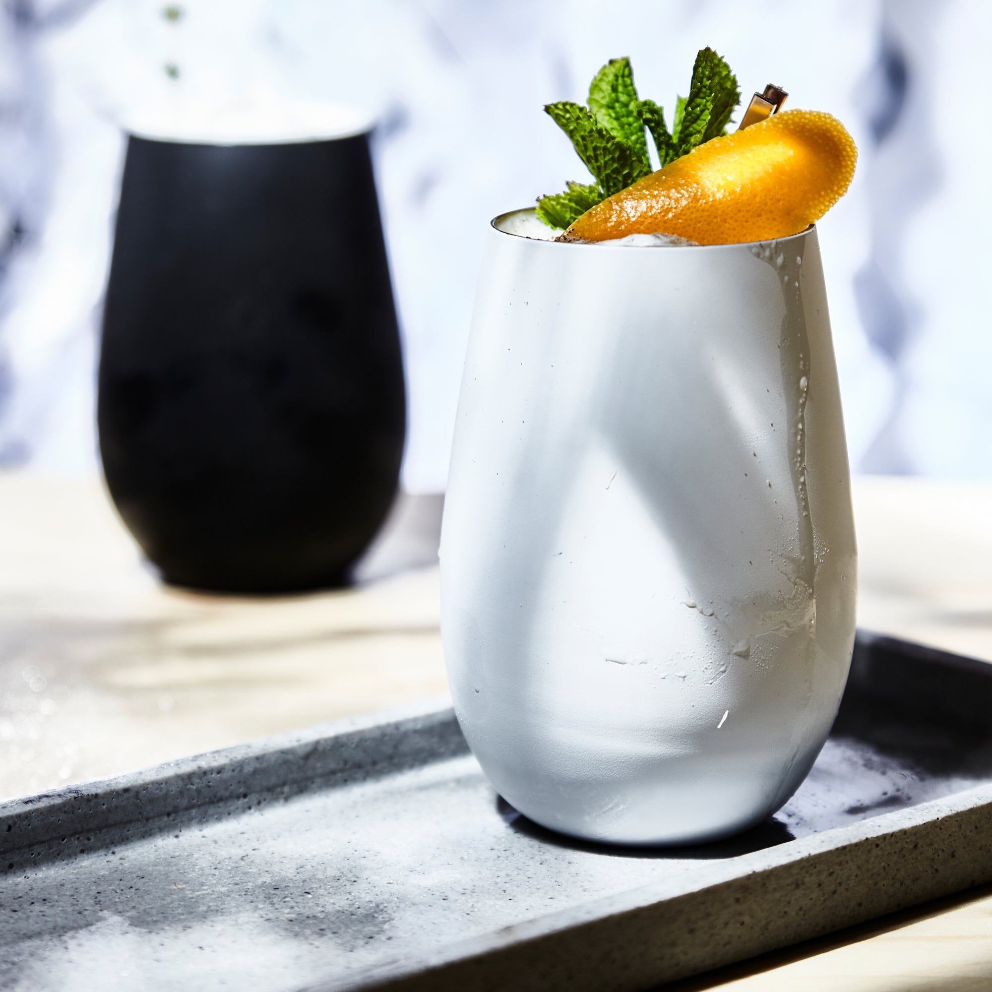 Hochwertige Designer Becher in elegantem Weiß mit frischen Minzblättern und Orange als Dekoration