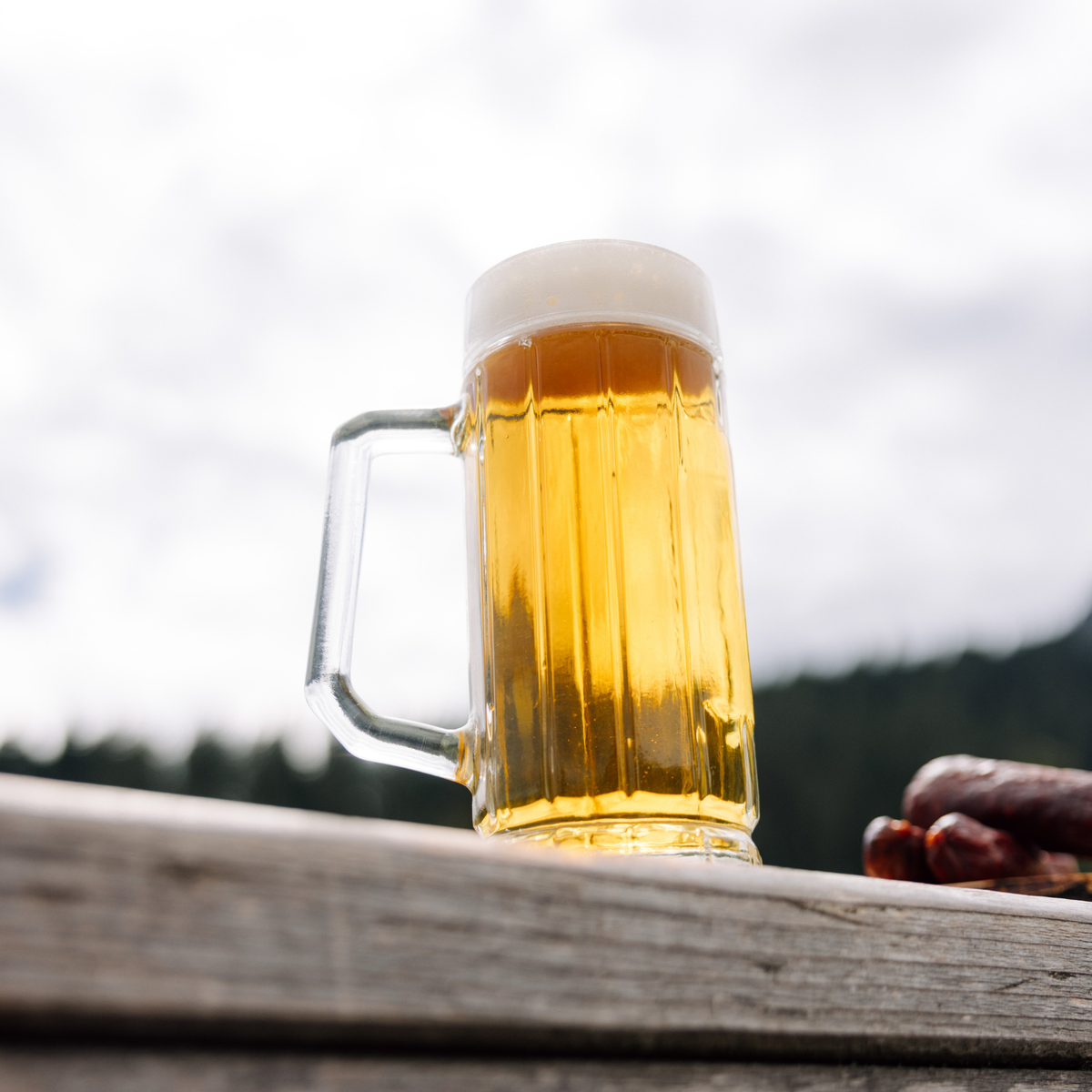 Oberglas Gambrinus Bierkrug 500ml, gefüllt mit Bier auf einem Holzzaun, der Himmel im Hintergrund