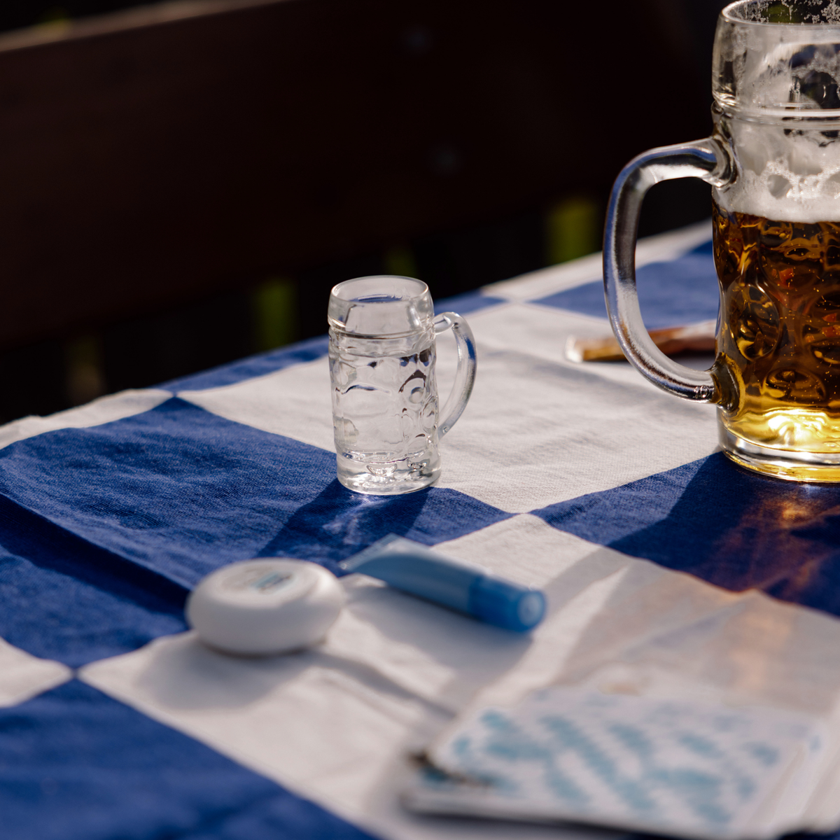 Oberglas Isar Schnapsglas 40 ml, zwei Gläser gefüllt, ein 40ml Glas mit einer klaren Flüssigkeit und ein 500ml Glas gefüllt mit Bier auf einer blau-weiß karierten Tischdecke